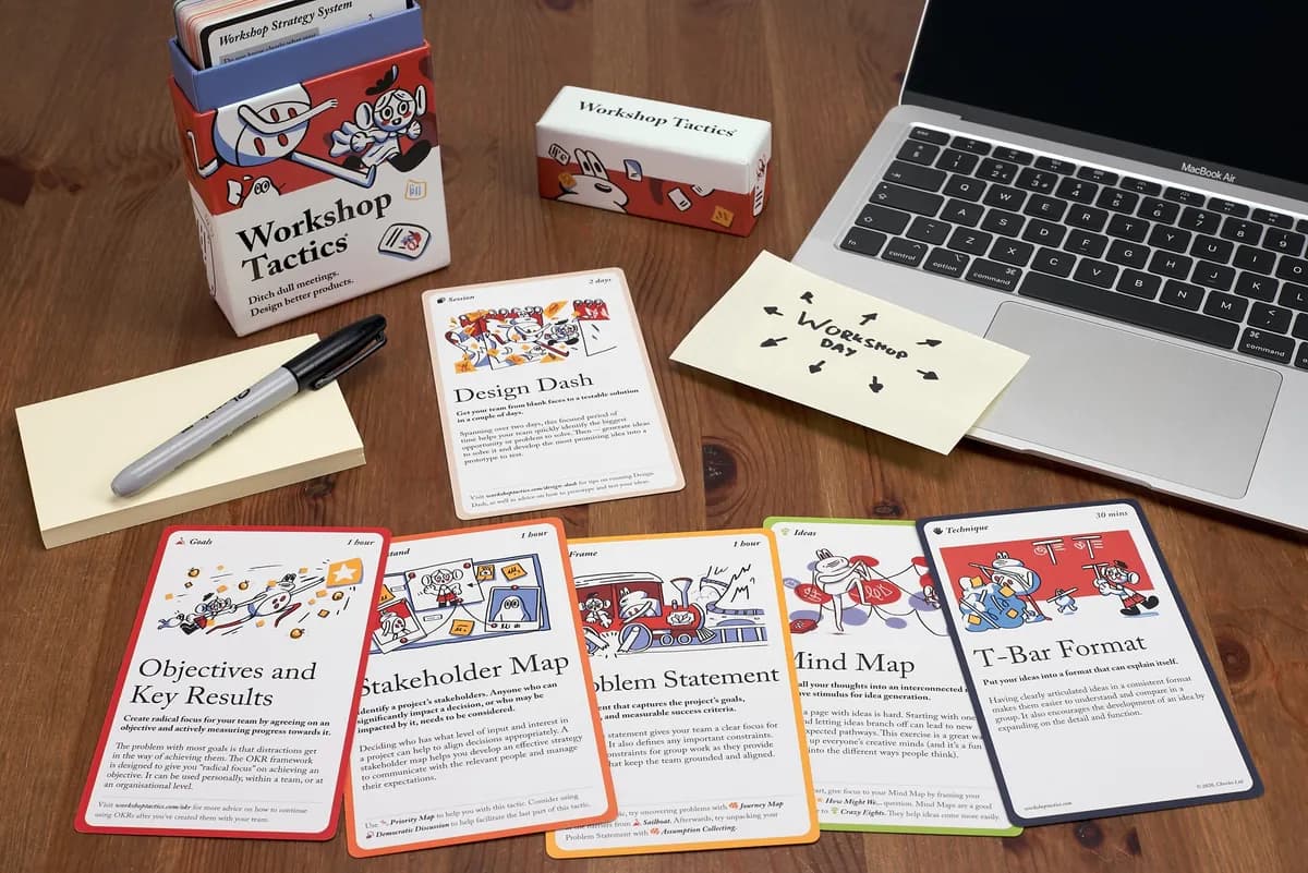 A Workshop Tactics deck on a wooden desk, its cards laid out beside a laptop
